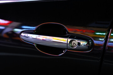Sleek Car Door Handle Reflecting City Lights at Night with Glossy Black Finish
