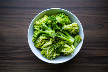 Bowl of fresh steamed broccoli on wooden table