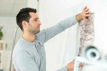 handyman putting up wallpaper on the white walls