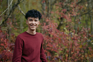 An authentic portrait of a young man outdoors, wearing a burgundy sweater, natural light, candid...