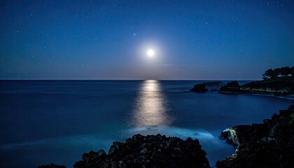 Majestic Seascape Under Moonlight Glowing Over Tranquil Dark Blue Ocean and Rocky Shoreline with Stars in the Night Sky