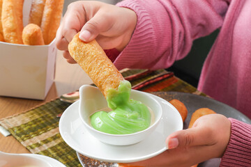 Fried Dough and Green Sauce: An individual dips a crispy fried dough stick into a creamy green sauce, creating a moment of deliciousness, perfect for foodies and culinary enthusiasts.