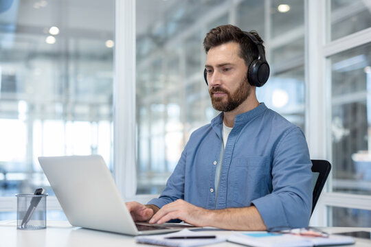 Focused man wearing headphones working on laptop in modern office