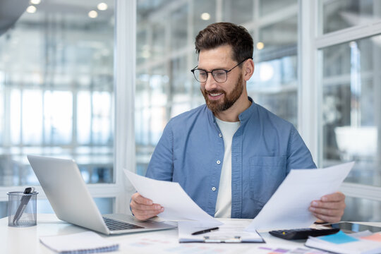 Businessman reading financial documents at office desk happily