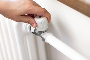 A man adjusts the temperature in his house using a radiator knob. Heating system, energy crisis, energy conservation, heat savings, heating season