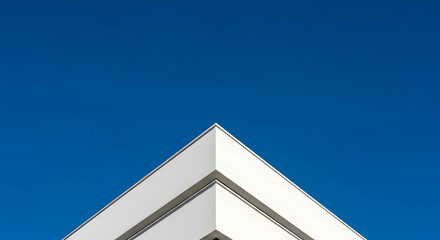 Sharp, clean lines of a modern white building corner create a geometric V-shape against a clear deep blue sky, an architectural abstract of simplicity