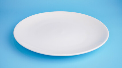 High angle view of empty ceramic white plate on blue background.