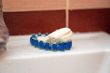A used white soap bar with foam residue in a blue silicone dish on ceramic sink