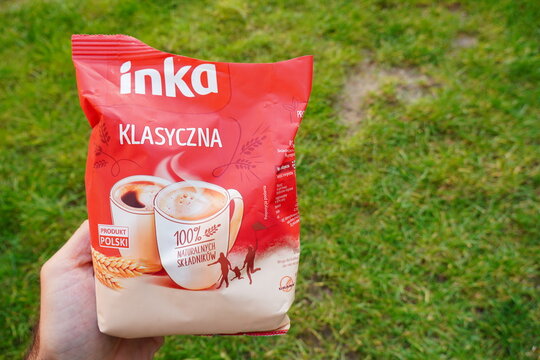 A hand holding a package of Inka classic 100% natural grain coffee substitute against a backdrop of green grass.