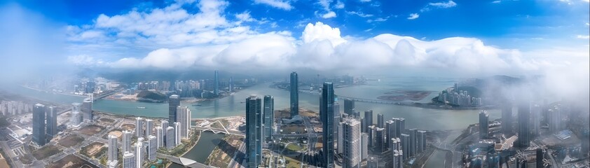 Obraz premium Dramatic Aerial Panoramic View of Modern Cityscape with Waterfront Bay and Skyscrapers Under Cloudy Sky