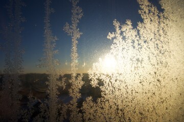 The dawn sun shines through a frost-covered window over the forest