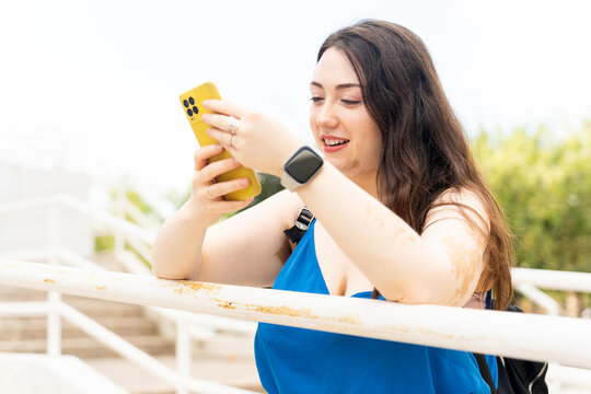 Smiling young woman with vitiligo using smartphone outdoors - Powered by Adobe