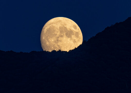 Harvest Super Moon   over the dark, silhouetted peaks, casting a soft glow on the rugged landscape,  Monte Bre, Lugano, Switzerland