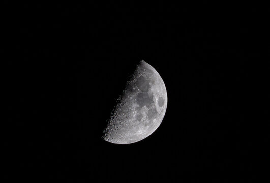 Aerial view of a half moon in the dark sky, revealing craters and textures, space.