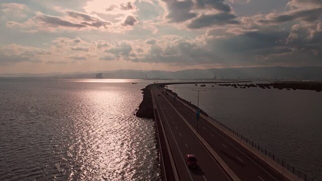 Stunning drone footage of a coastal highway bridge over water at sunset with shimmering reflections and mountain backdrop, ideal for travel, cinematic, and infrastructure projects.
