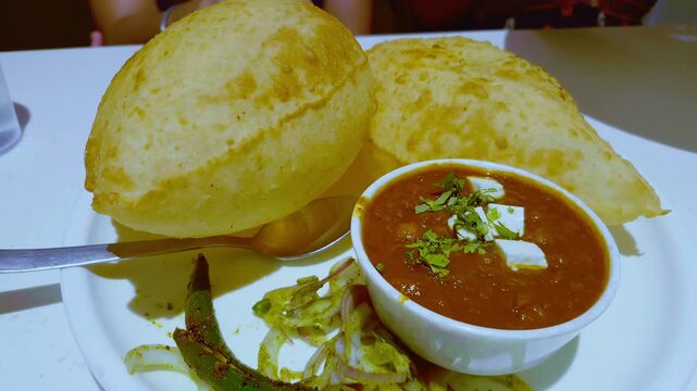 A plate of chole bhature is served with cheese and a side of chilli pickle for added flavor and spice.