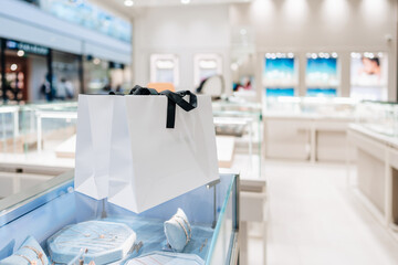 White shopping bags with black ribbon handles are placed on a glass jewelry display case inside a...