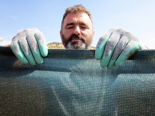 A man ties a shade net to his garden. It is used in gardening, nurseries and agriculture.