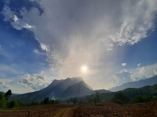 Dramatic sky over majestic mountain peak at sunrise brings sense of awe and tranquility, with sunrays breaking through clouds creating breathtaking natural spectacle