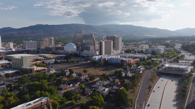 Aerial view of Reno, Nevada, at sunset with casino skyline, National Bowling Stadium, Sierra Nevada mountains, and active highway traffic below.