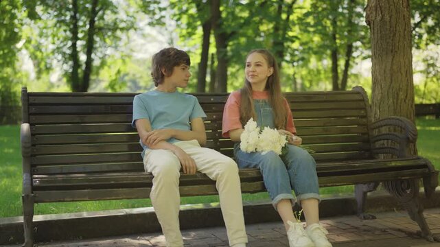 Happy teenage couple talking on park bench, first love, cute dating moments