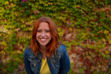 Young woman with red hair smiling broadly, feeling joy and happiness outdoors during an autumn day