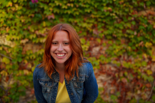 Young woman with red hair smiling broadly, feeling joy and happiness outdoors during an autumn day
