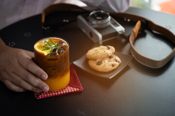 Top view of a hot black coffee in a white cup and saucer, two chocolate chip cookies, a vintage film camera with a leather strap, relaxation, hobbies, creativity, and a cozy break moment.