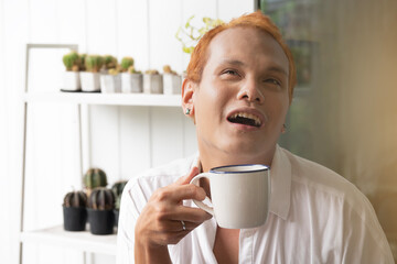 Asian man with dyed blonde hair enjoys a warm and satisfying morning coffee.