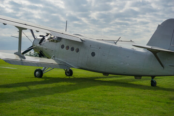 Old-fashioned silver propeller aircraft parked on a green grassy airfield AN2 under a cloudy sky, showcasing aviation history and retro design.