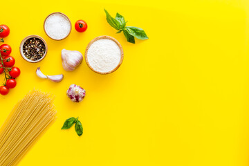 Flat lay of uncooked spaghetti with ingredients for cooking Italian pasta - tomatoes and basil with garlic - on a yellow background, top view