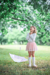 Little girl standing next to a closed umbrella on the grass with a shocked expression on her face. A raw and vivid emotional reaction during a playful rainy-day moment.