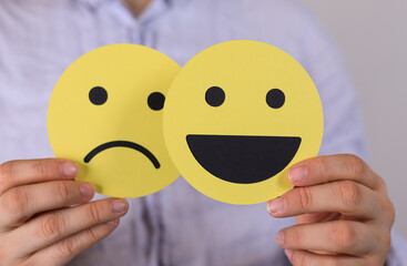 Stock photo of hands holding sad and happy emoticons.  Concepts: emotions, mood, choice, feeling,...