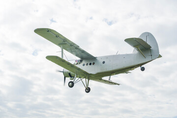 grey an 2 biplane taking off or landing above a green field against a cloudy sky, scene of aviation technology, concept of agriculture, cargo transport, retro travel