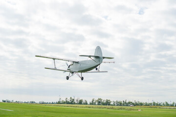 grey an 2 biplane taking off or landing above a green field against a cloudy sky, scene of aviation technology, concept of agriculture, cargo transport, retro travel © Lana Pietukhova