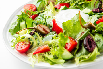Fresh mixed salad with cherry tomatoes, cucumbers, bell peppers, olives, caper berries, and creamy cheese on a white plate. Colorful, healthy, and appetizing vegetarian dish