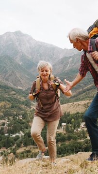 Vertical slow motion video mature couple trekking mountains with backpacks symbol family love relationship support healthy lifestyle active retirement travel freedom nature adventure together