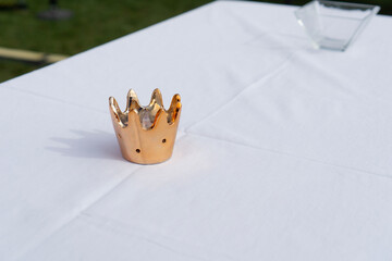 close up of a gold crown shaped candle holder resting on a white tablecloth with copyspace, scene of festive table decoration, concept of royal celebration, wedding decor