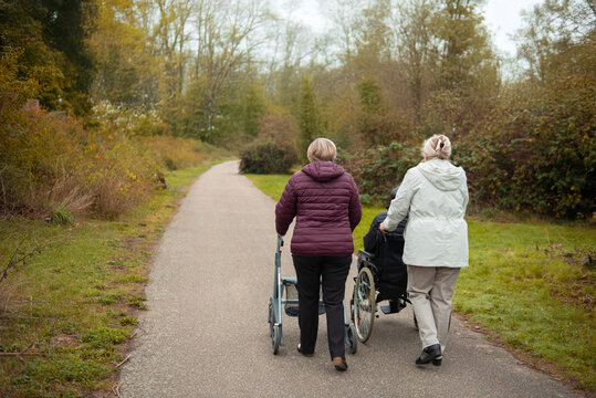 Elderly people taking a walk with help of walker with friends on a cold day through the park