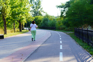 Woman walking alone on a scenic path in a green park during a sunny afternoon in early summer