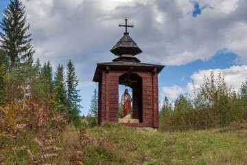 Small wooden wayside Christian chapel with statue of Jesus inside