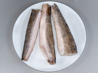 Frozen Argentine hakes on plate on gray surface, top view