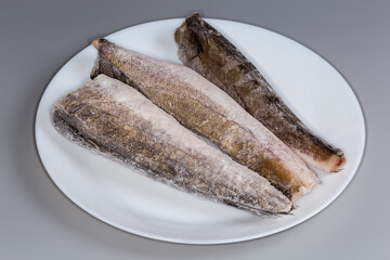 Frozen Argentine hake carcasses on plate on a gray background