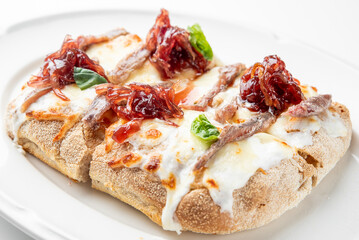 Gourmet pizza with anchovies, caramelized onions, mozzarella, and basil on rustic crust, served on white plate. Close-up, artisanal food styling, top view