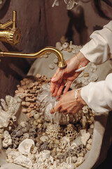 Young woman washes her hands in a seashell decorated washbasin with unique pearl beads