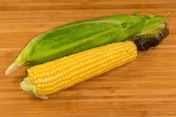 Peeled and unpeeled raw sweet corn ears on cutting board