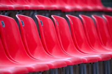 Close view of empty red plastic stadium seats in a single curved row, numbers visible. Repetition and shallow depth of field create a clean abstract sports-venue pattern.