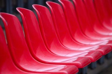 Abstract close-up of glossy red stadium seats forming a rhythmic curve. Selective focus and repetition create a clean graphic pattern. Empty grandstand, no people.