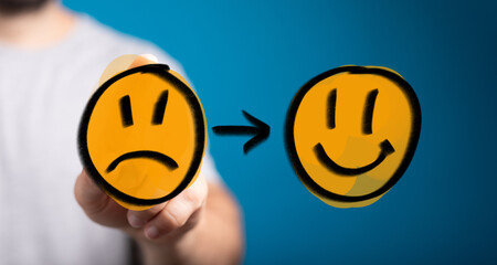 Conceptual image showing a hand transforming a sad emoji into a happy emoji, symbolizing positive...