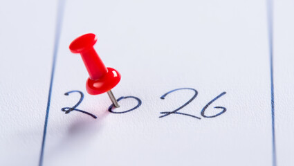 A crisp image of the number "2026" written in black ink, with a red pushpin pointing to it. Ideal for concepts related to future planning, goals, and events in the new year